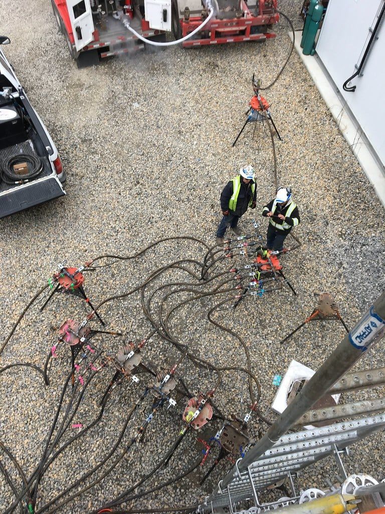 Overhead view of test hoses and manifolds laid out across a gravel pad