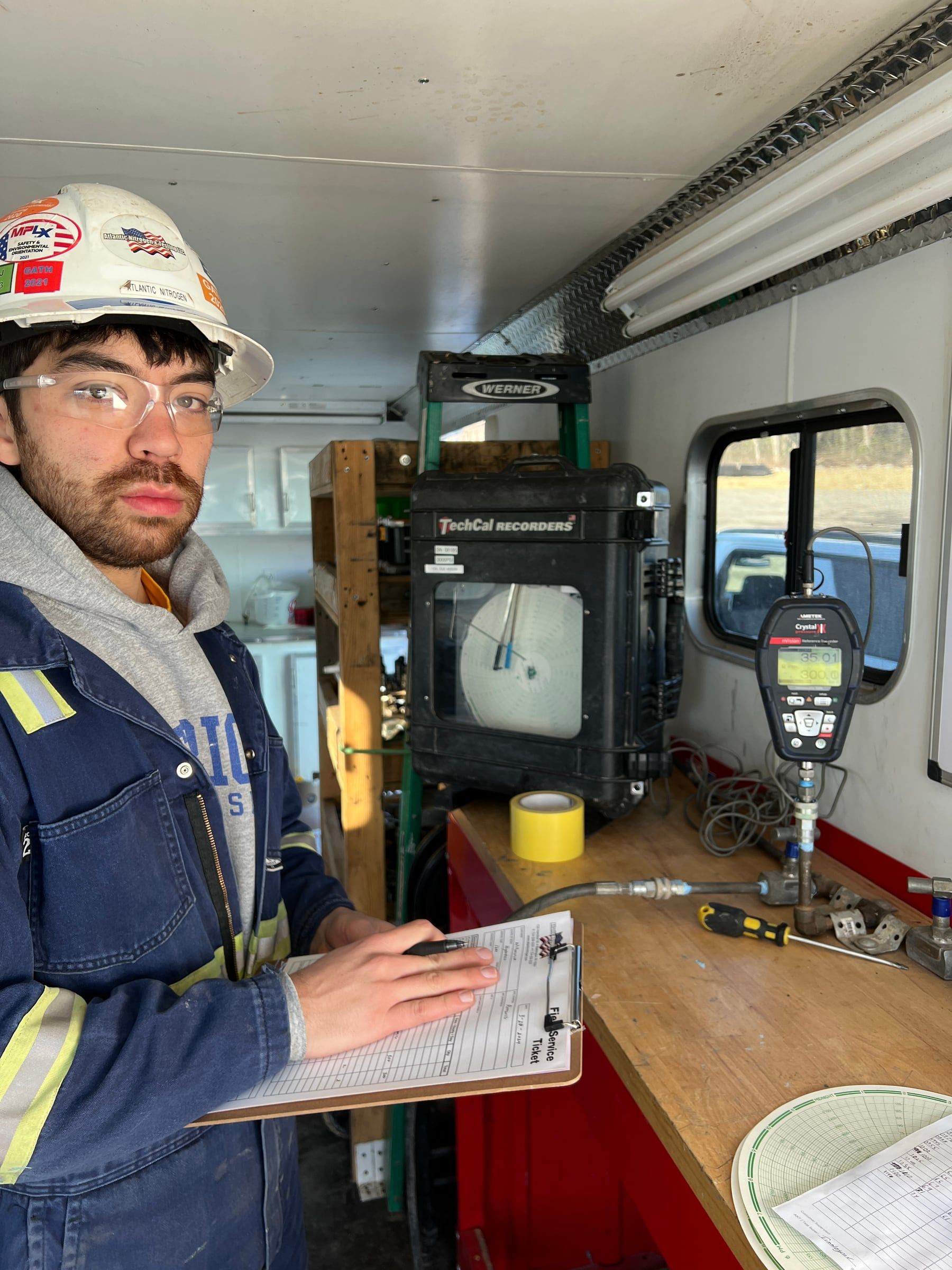 Technician recording readings on a clipboard beneath a pipe spool during rig in