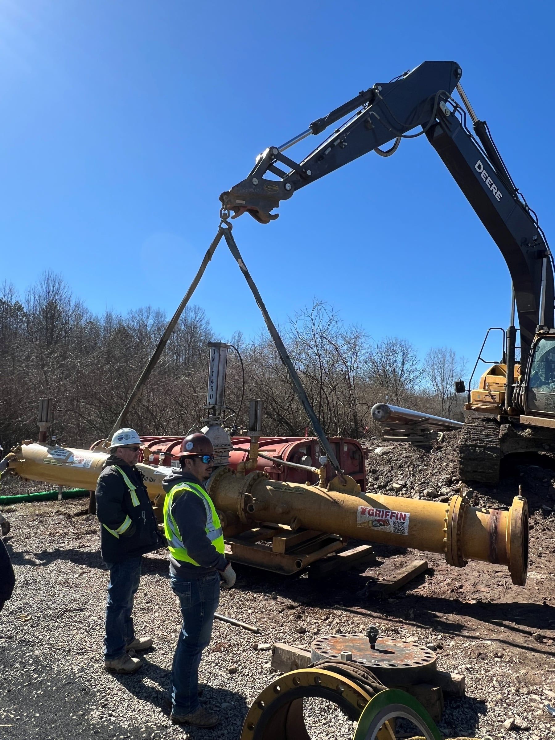 Two crew members rigging in a test head on a 20 inch line while an excavator holds the spool